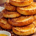 Stack of freshly toasted brioche burger buns on a wooden board, showing golden crispy edges and melted butter coating