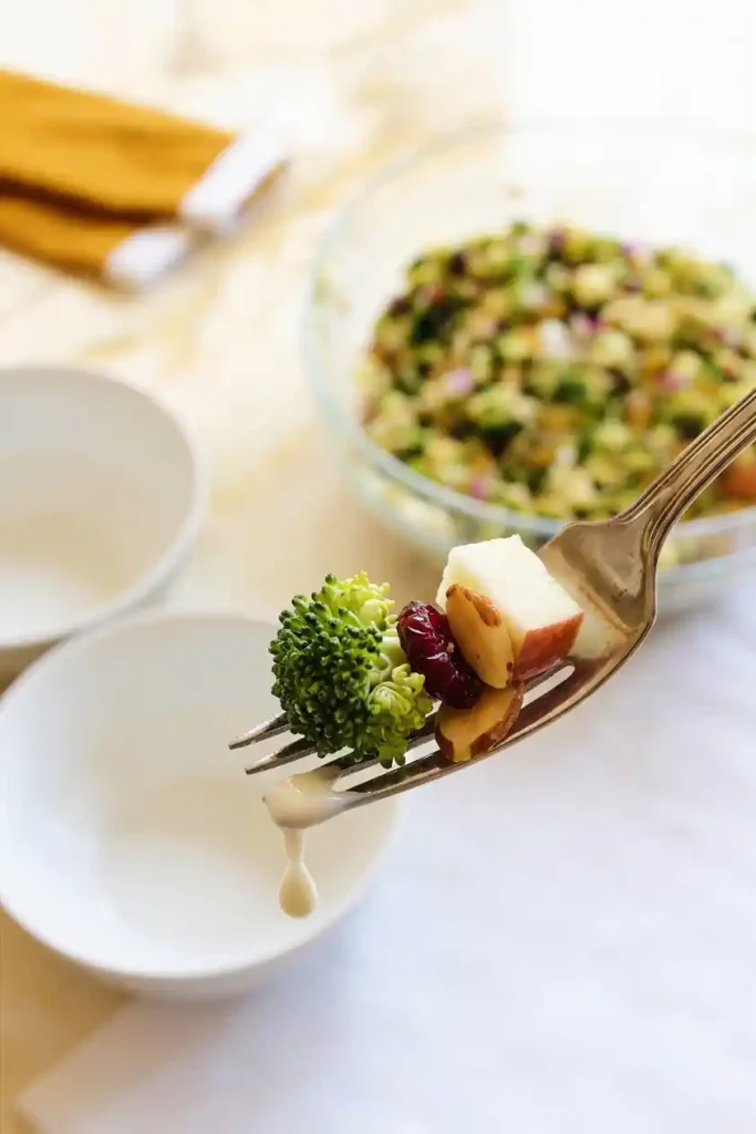 Close-up of a fork holding broccoli, apple, almond, and cranberry pieces in Broccoli Salad, showcasing vibrant ingredients with creamy dressing
