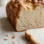Fluffy Keto Cottage Cheese Cloud Bread loaf with a slice, showcasing airy crumb and golden-brown crust on a neutral cloth with blurred floral background