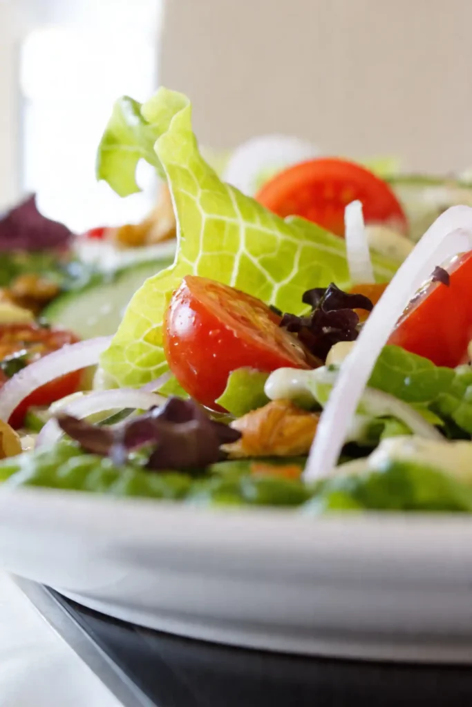 Macro shot of Little Gem salad highlighting crisp lettuce veins, juicy cherry tomato, sliced red onion, and creamy dressing drizzle