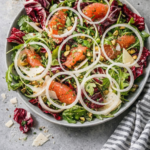 Radicchio salad featuring circular onion rings arranged over grapefruit, radicchio, arugula, and pistachios