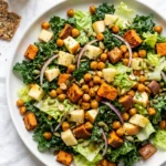 Plated kale sweet potato salad topped with roasted chickpeas, diced apples, red onion slices, and pumpkin seeds