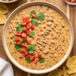 Creamy Rotel dip served in rustic ceramic bowl on wooden board. Topped with diced tomatoes and fresh cilantro leaves. Surrounding the bowl are tortilla chips, a small glass dish of extra pico de gallo, and scattered cilantro sprigs. White linen napkin tucked at corner. Perfect party appetizer or game day snack