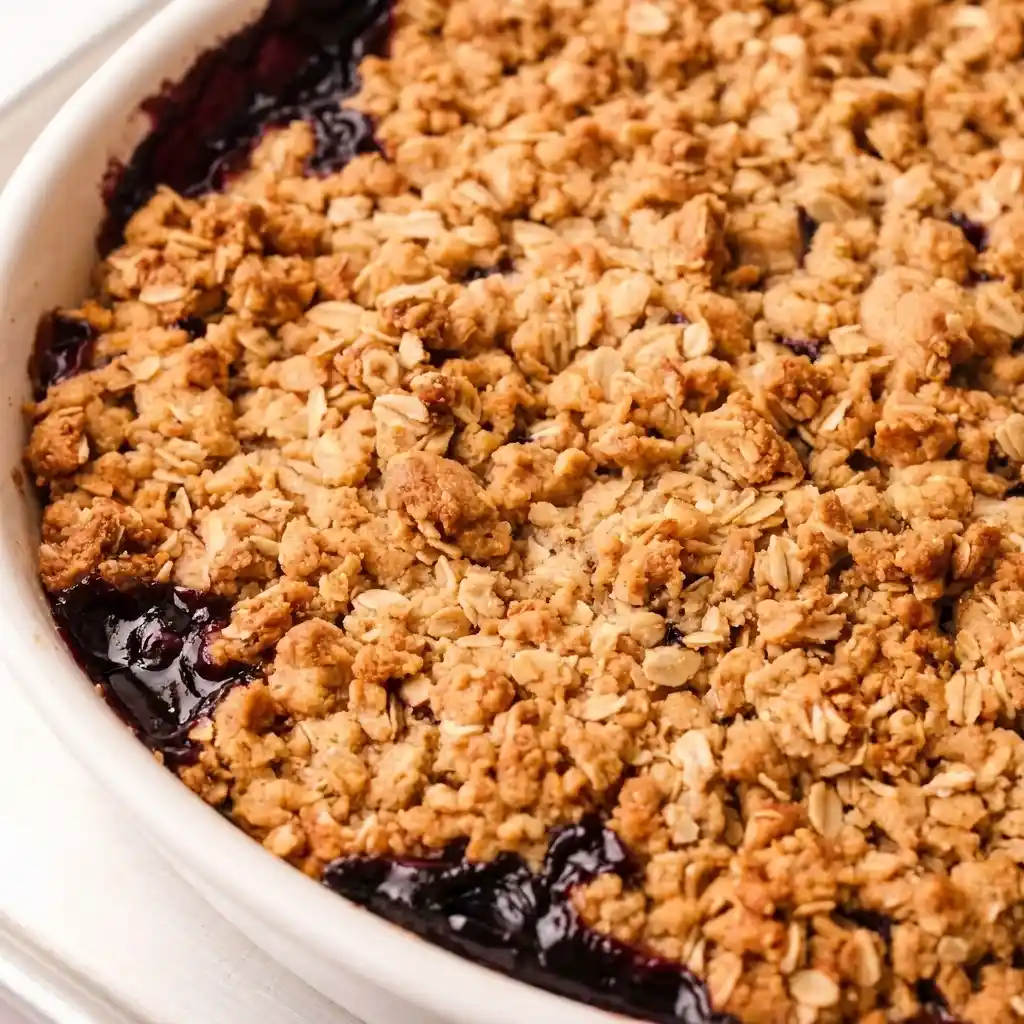 Close-up of baked apple blueberry crisp with golden oat topping and bubbling fruit filling in white dish