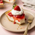 Slice of creamy strawberry pie with graham cracker crust and glaze on a plate next to a gold fork.